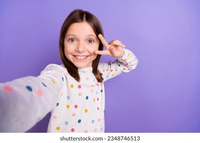 Photo of friendly excited little girl dressed dotted pullover showing v-sign cover eye recording video vlogging isolated purple color background