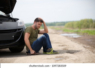 Photo Of Frustrated Man Sitting Next To Broken Car With Open Hood