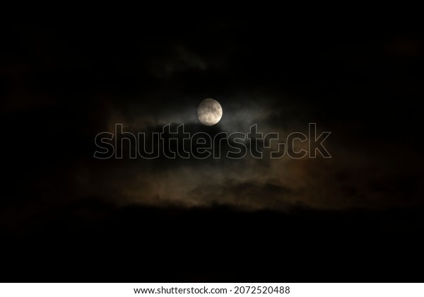 Photo of the full moon. A\
large moon in a black sky without stars surrounded by beautiful\
clouds.