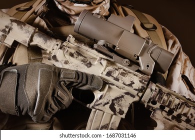 Photo of a fully equipped desert soldier holding automatic rifle with clip on dark brown background.