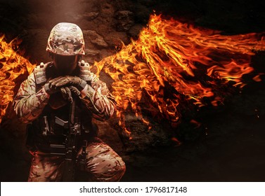 Photo of a fully equipped military soldier in helmet, armor vest and rifle kneeling with fire wings behind him.