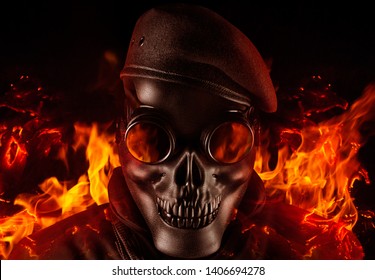 Photo of a fully equipped soldier in black armor tactical vest standing in skull mask and beret on black background with flying ashes and fire closeup front view.