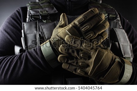 Photo of a fully equipped soldier in black armor tactical vest and gloves standing on black background closeup front view.