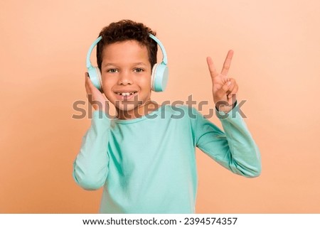 Photo of funky charming cheerful boy wear stylish clothes enjoy stereo audio v-sign cool party isolated on beige color background