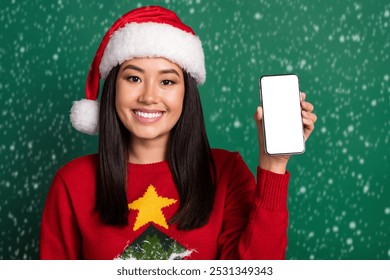 Photo of funky cheerful girl dressed ugly print red x-mas pullover headwear showing modern gadget empty space isolated green color background - Powered by Shutterstock