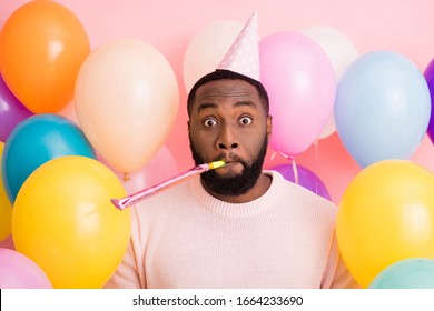 Photo Of Funky Dark Skin Guy Birthday Surprise Party Surrounded Many Balloons Blowing Noisemaker Crazy Guest Wear Paper Cone Cap Sweater On Pink Color Background