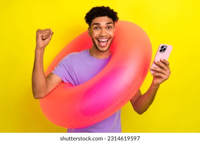 Photo of funky delighted person hold inflatable circle use smart phone raise fist shout yes hooray isolated on yellow color background - Shutterstock ID 2314619597