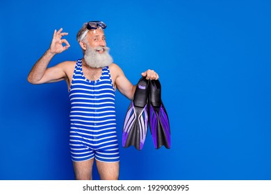 Photo Of Funky Funny Mature Smiling Man Hold Slippers Showing Okay Sign Prepare To Swim Isolated On Blue Color Background