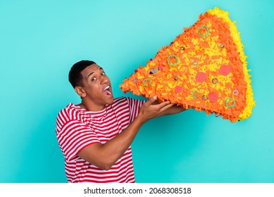 Photo of funky funny young man wear striped t-shirt smiling biting huge pizza slice isolated teal color background