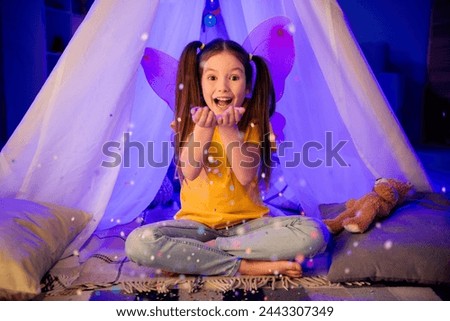 Photo of funky impressed small preteen girl wear casual style wings throwing sparkles sitting hovel indoors room home house