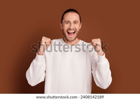 Photo of funky lucky man wear white sweater rising fists shouting yes isolated brown color background