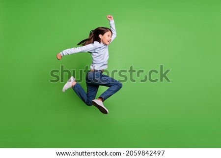 Photo of funky pretty schoolgirl wear blue turtleneck jumping high running fast empty space smiling isolated green color background