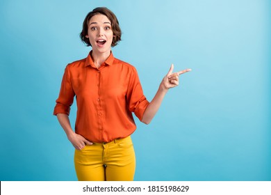 Photo Of Funny Attractive Pretty Lady Direct Index Finger Side Empty Space Show Low Prices Season Banner Good News Wear Orange Office Shirt Yellow Trousers Isolated Blue Color Background