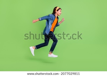 Photo of funny charming student girl wear denim shirt smiling jumping high running fast isolated green color background