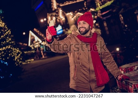 Photo of funny cheerful guy dressed coat recording video x-mas vlog modern device outdoors urban fair park