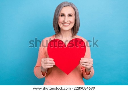 Photo of funny cheerful woman wear coral shirt smiling holding red paper heart isolated blue color background