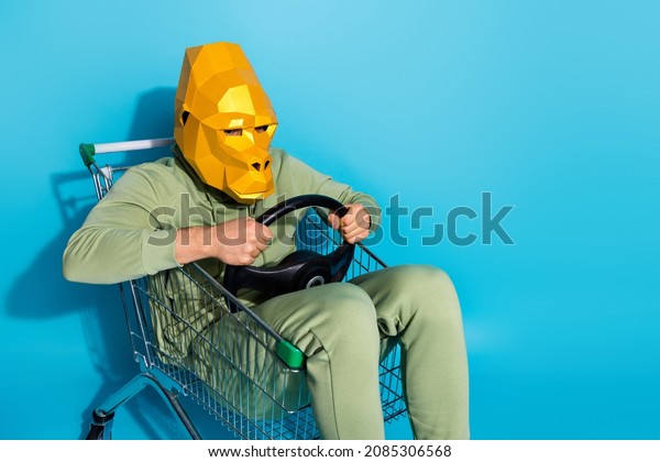 Photo\
of funny confident guy dressed wild animal mask riding shopping\
trolley empty space isolated blue color\
background