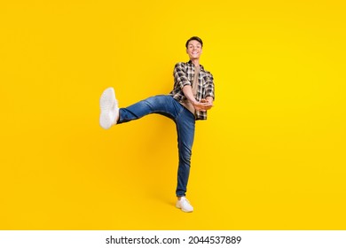 Photo of funny crazy guy dance hold hands raise leg wear plaid shirt jeans sneakers isolated yellow color background - Shutterstock ID 2044537889