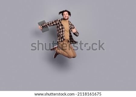 Photo of funny cute guy dressed checkered shirt jumping holding device thumb up isolated grey color background