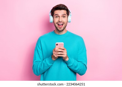 Photo of funny excited young man overjoyed shocked cheap itunes subscription hold phone listen headphones isolated on pink color background