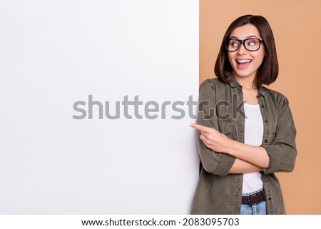 Photo of funny lady indicate finger poster empty space wear glasses khaki shirt isolated beige color background Imagine de stoc © 
