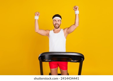 Photo of funny lucky guy sportswear rising fists winning treadmill race isolated yellow color background