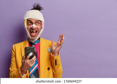 Photo Of Funny Man With Missing Teeth, Has Bruises Under Eyes, Beaten During Corporative Party, Sort Out Relationships With Someone, Uses Mobile Phone For Surfing Net, Isolated On Purple Background