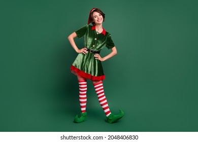 Photo of funny positive cheerful helper lady hands hips wear elf costume hat stockings isolated green color background