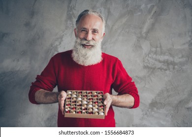 Photo Of Funny Positive White Haired Old Man Holding Box Of Colorful Little X-mas Tree Decor Balls Wear Red Knitted Pullover Hipster Outfit Isolated Grey Color Wall Background