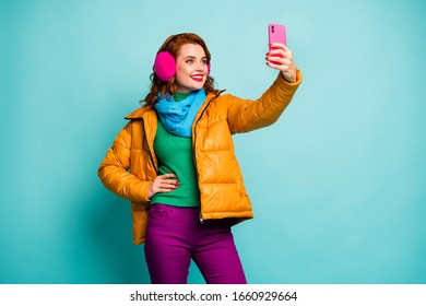 Photo of funny pretty lady hold telephone hands taking selfies wear trendy casual ear covers yellow overcoat scarf magenta pants sweater isolated teal color background - Powered by Shutterstock