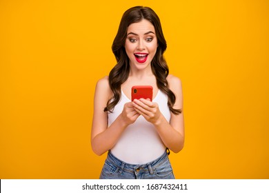 Photo of funny pretty lady hold telephone hands open mouth read cool comments youth blog followers wear white tank-top jeans isolated bright yellow color background