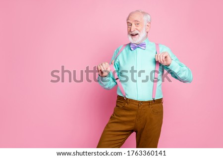 Photo of funny stylish grandpa positive emotions before senior party meeting touch hold fingers suspenders wear shirt violet bow tie brown pants isolated pink pastel color background