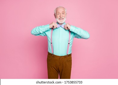 Photo Of Funny Stylish Look Grandpa Hold Hands Buttoning Necktie Positive Emotions Before Senior Party Wear Shirt Suspenders Violet Bow Tie Pants Isolated Pastel Pink Color Background