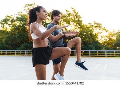 Photo Of Funny Young Couple In Sportswear Doing Exercise And Smiling While Working Out At Playground Outdoors