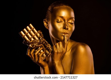 Photo Of Gentle Lady Body Painted Gold Shimmer Eyes Closed Touch Her Lip Hold Chocolate Bar Isolated Dark Background