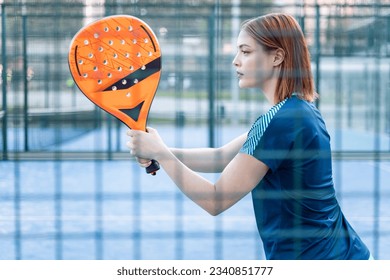 Photo of a girl behind a fence of an outdoor paddle tennis court that is posing with a racket to receive a serve. Concept of women playing paddle. Paddle for women.