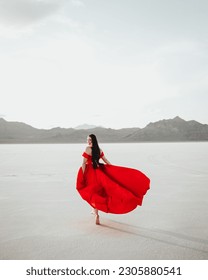 Photo of a girl in a long red dress at the Bonneville Salt Flats in Utah. Dress is flowing in the wind and the girl is looking back and smiling at the camera.