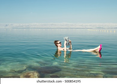Foto da menina lendo jornal flutuando na superfície Mar Morto desfrutar de sol de verão e férias. Turismo recreativo, estilo de vida saudável, conceito de tempo livre
