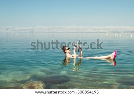 Photo of the Girl reading newspaper floating on surface Dead Sea enjoy summer sun and vacation. Recreation tourism, healthy lifestyle, free time concept