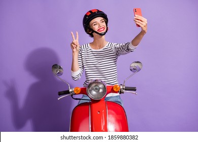 Photo of girl ride moped make selfie phone show v-sign wear helmet striped shirt isolated violet color background