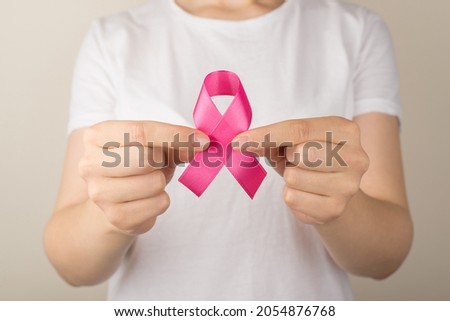 Photo of girl in white t-shirt demonstrating vivid pink ribbon symbol of breast cancer awareness on isolated grey background