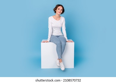 Photo of girlish adorable woman wear white shirt sitting white cube chair isolated blue color background - Shutterstock ID 2108570732