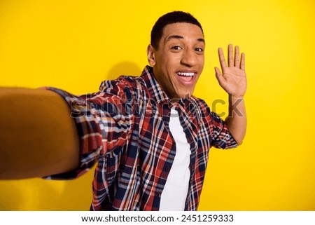 Photo of glad attractive friendly man wear trendy plaid clothes waving hand live stream make selfie isolated on yellow color background