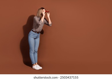 Photo of glad cheerful woman wear checkered stylish clothes hand hold binoculars look empty space isolated on brown color background - Powered by Shutterstock