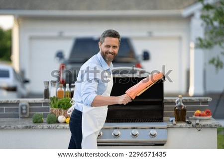 photo of glad man barbecuing trout fillet on grill. man barbecuing trout fillet. man barbecuing