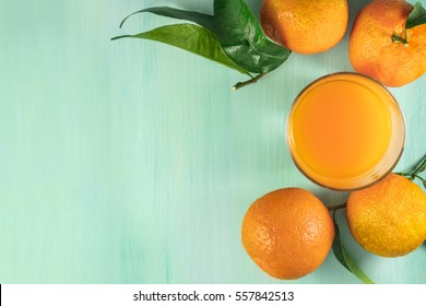 A Photo Of A Glass Of Citrus Juice With Vibrant Orange Tangerines With Green Leaves, Shot From Above On A Light Background Texture With Copy Space. Selective Focus