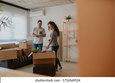 Photo of good looking young couple having fun while unpacking boxes in new home on moving day. Young couple is moving in to their new home.