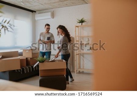 Photo of good looking young couple having fun while unpacking boxes in new home on moving day. Young couple is moving in to their new home.