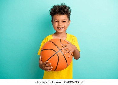 Photo of good mood positive schoolboy with brown hair dressed yellow t-shirt hold basketball ball isolated on turquoise color background