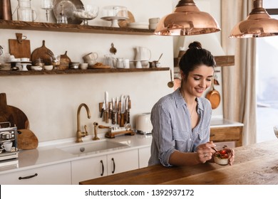 Photo Of Gorgeous Brunette Woman 20s Eating Panna Cotta Dessert With Teaspoon While Having Breakfast In Stylish Kitchen At Home